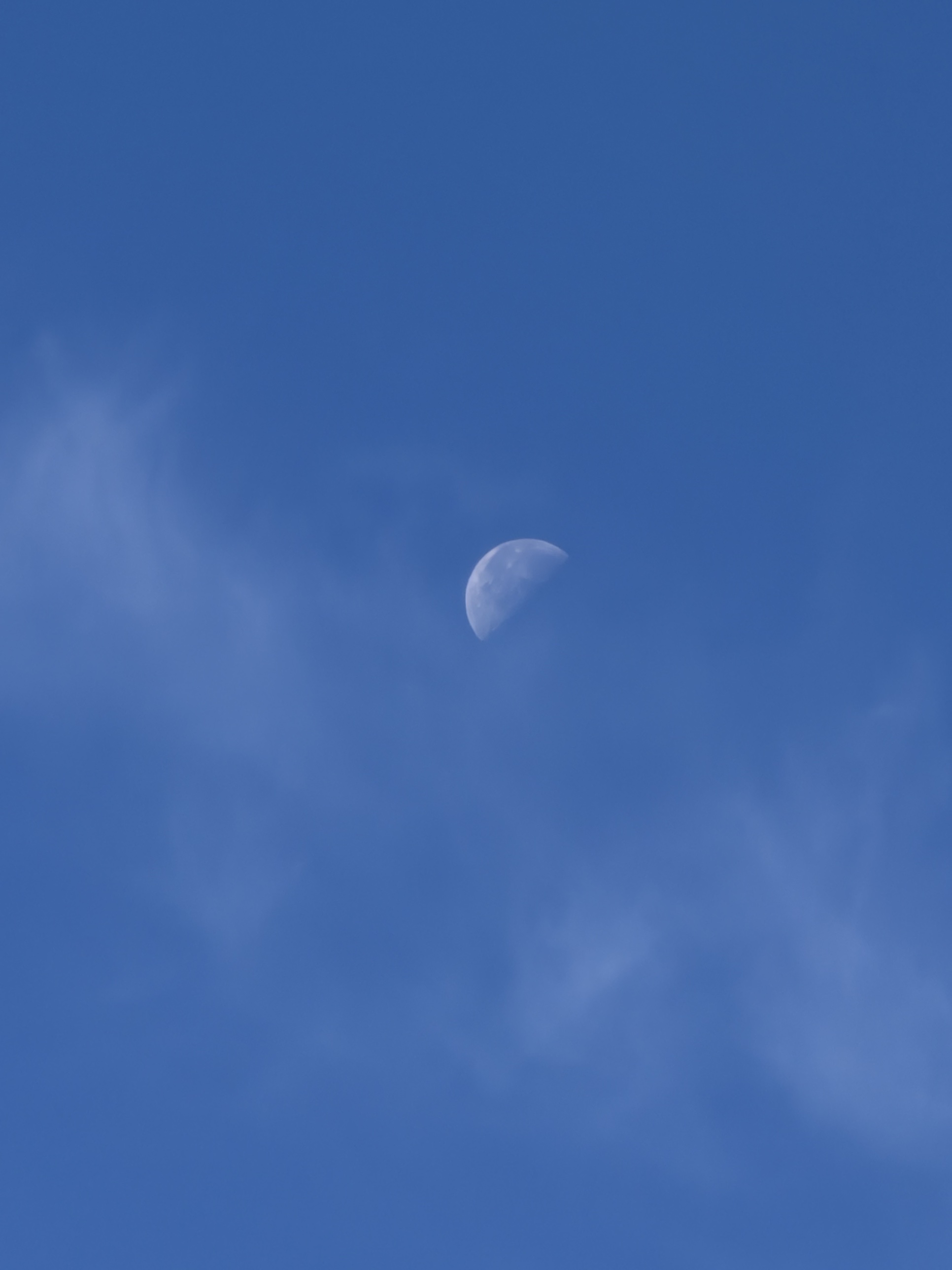 A half moon in a deep blue daytime sky with thin wisps of cloud